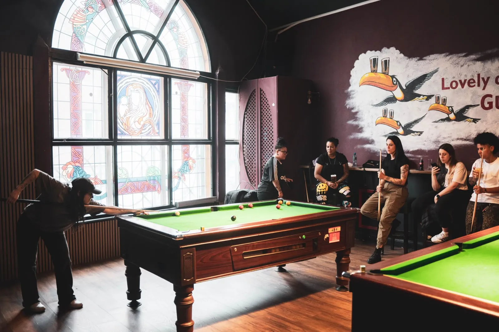 Group enjoying a game of pool by the stained-glass window at Plunkets Dublin